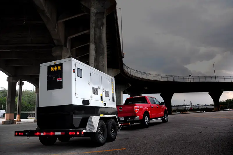 Red pickup truck towing a generator under overpass.